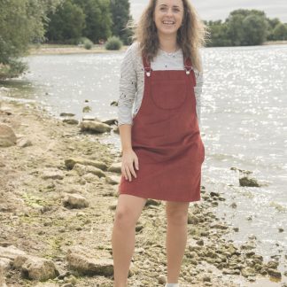 Woman wearing the Emily Dungaree Dress sewing pattern by Bobbins and Buttons. A pinafore dress pattern made in denim, needle cord, jumbo cord, linen or medium weight woven blend fabrics, featuring an A-line silhouette, no zips, in-seam and patch pockets with an above knee finish.