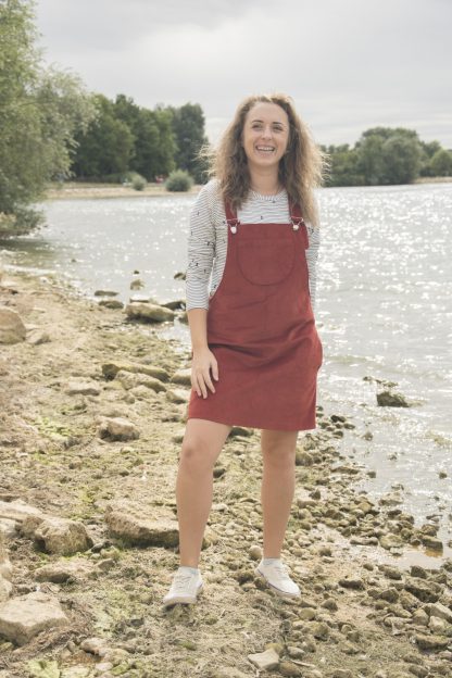 Woman wearing the Emily Dungaree Dress sewing pattern by Bobbins and Buttons. A pinafore dress pattern made in denim, needle cord, jumbo cord, linen or medium weight woven blend fabrics, featuring an A-line silhouette, no zips, in-seam and patch pockets with an above knee finish.