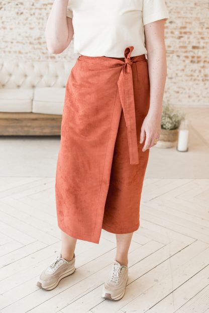 Woman wearing the Katya Skirt sewing pattern from Lenaline Patterns on The Fold Line. A wrap skirt pattern made in suede, denim, gabardine, velvet, chambray or jacquard fabrics, featuring an apron-style, front and back waist darts, waistband with hidden button extending into a self-fastening belt and midi length hem.