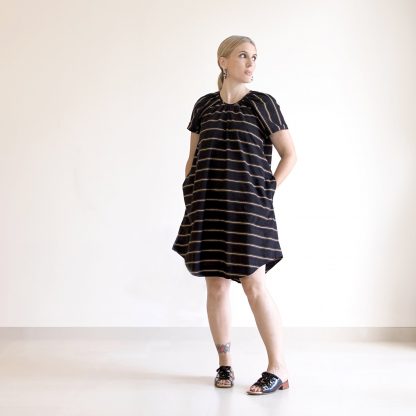 Woman wearing the Calyx Smock sewing pattern from Pattern Fantastique on The Fold Line. A dress pattern made in woven fabrics, featuring a gathered neckline, relaxed fit, above knee length, shirttail hemline, cap sleeves and tie closure at the centre back.