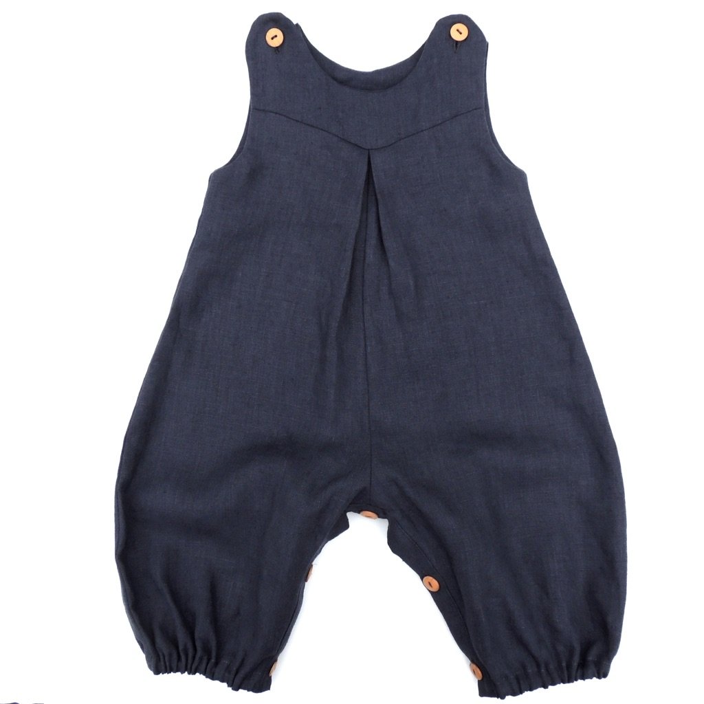 The Babies' Penny Romper sewing pattern by Dhurata Davies Patterns. A romper pattern made in light to medium weight woven fabric, featuring snap fasteners on the shoulders and leg inseam, a front V shaped yoke, inverted front pleat detail, all-in-one sleeve and elasticated hems.