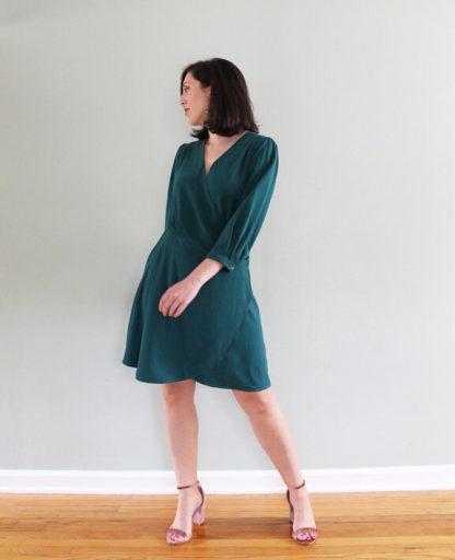 Women wearing the Romy Wrap Dress sewing pattern from Pattern Scout on The Fold Line. A wrap dress pattern made in lightweight weight woven fabrics, featuring shoulder and waist pleats, ¾ length sleeves with button cuff, knee length hem, waist button closure and curved high-low hemline.
