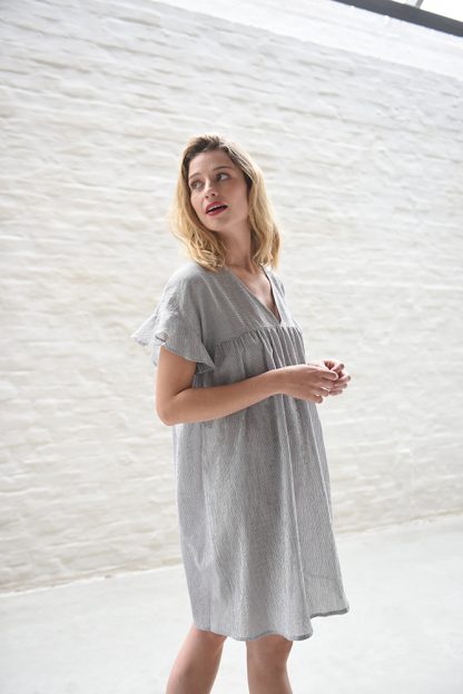 Woman wearing the Rosalie Dress sewing pattern from Fibre Mood on The Fold Line. A dress pattern made in cotton, poplin or linen blend fabrics, featuring a babydoll style, deep V-neck, short ruffled sleeves, roomy fit, above knee length, front and back yoke with gathers.