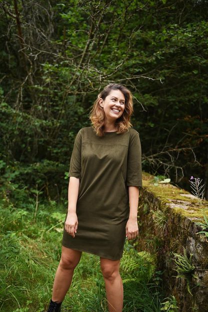 Woman wearing the Gusta Dress sewing pattern from Fibre Mood on The Fold Line. A dress pattern made in wovens, knits, interlock, ponte roma, jacquard jersey or neoprene fabrics, featuring a straight cut, round neck, elbow length sleeves, above knee length finish, front yoke and pockets.