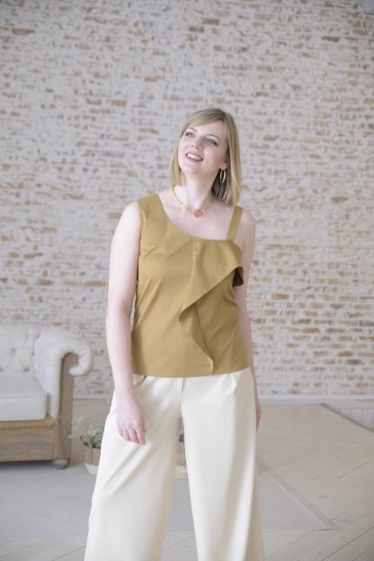 Woman wearing the Ylia Top sewing pattern from Lenaline Patterns on The Fold Line. A top pattern made in cotton, linen, viscose, cotton plumetis, thin wool or denim fabrics, featuring an asymmetrical neckline, front bodice ruffle, one narrow and one broad shoulder strap.