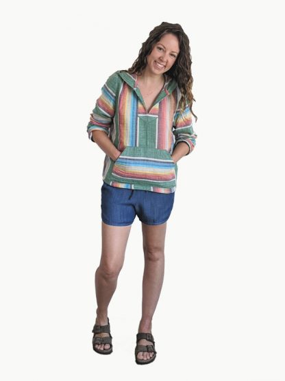 Woman wearing the Vero Beach Set sewing pattern from Hey June Handmade on The Fold Line. A hoodie and shorts pattern made in linen or linen blends, cotton, cotton blends, and rayon blend fabrics, featuring a relaxed-fit hoodie with front placket, kangaroo pocket, and extra-long sleeves. Shorts are fitted, elastic-waist, mid-rise shorts, front hip pockets, back darts, large back patch pocket, and bias finished tulip hem.
