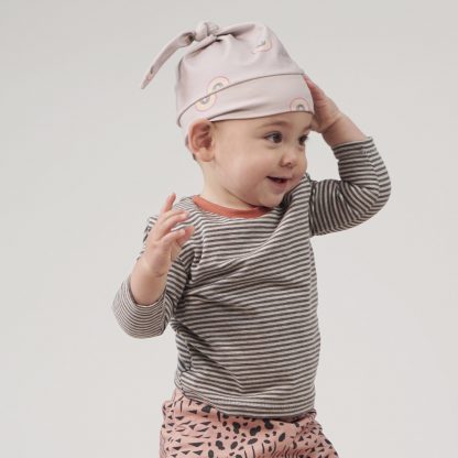 Baby wearing the Baby's Nolan Knot Hat sewing pattern from Pattern Paper Scissors on The Fold Line. A hat pattern made in jersey, knit or cotton elastane fabrics, featuring a stretch fit, deep band and tied top knot.