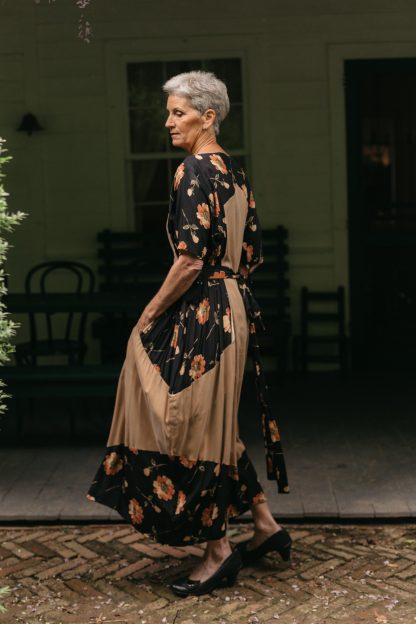 Woman wearing the 261 Paris Promenade Dress sewing pattern from Folkwear on The Fold Line. A dress pattern made in silk, silk velvet, rayon, feather-weight cotton, or jersey, crisp cotton, lightweight linen, and silk taffeta fabrics, featuring a relaxed fit, bateau neckline, elbow length sleeves, high-low hem, midi length, and bib-shaped overdress.