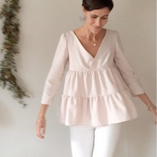 Woman wearing the Eugénie Blouse sewing pattern by Atelier Scammit. A blouse pattern made in very light to medium batiste, crepe, light denim or flannel fabrics, featuring ruffled sleeves, wrap V-neckline, smocking and tiers.