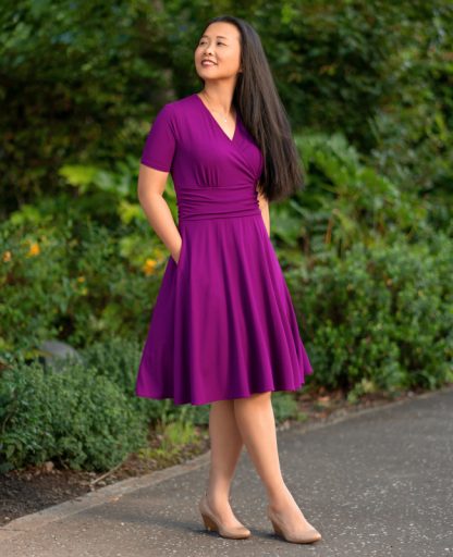 Woman wearing the Antrim Dress sewing pattern from Itch to Stitch on The Fold Line. A dress pattern made in lightweight to medium weight knit fabrics, featuring a fit-and-flare style, surplice front bodice, short sleeves, gathered waistband, half-circle skirt, below knee length, in-seam pockets, pullover style, and bust cup options.