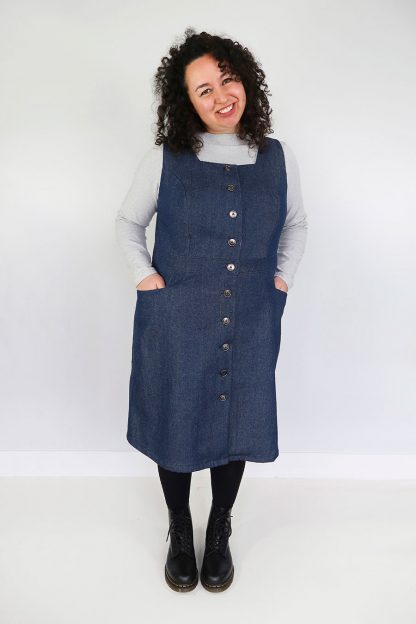 Woman wearing the Dulcie Pinafore sewing pattern from Jennifer Lauren Handmade on The Fold Line. A pinafore dress pattern made in denim, corduroy, wool, suitings, tweeds and mammoth flannel fabrics, featuring a button-front, square neckline, semi-fitted A-line skirt, square in-set pockets, princess seams, fully lined bodice, optional topstitching, and knee length.