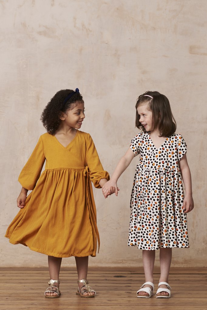 Children wearing the Child/Teen Little Hannah Dress sewing pattern from By Hand London. A dress pattern made in cottons, linens, silks or viscose, featuring a scoop wrap neckline, gathered skirt, short or long sleeves and no zipper.