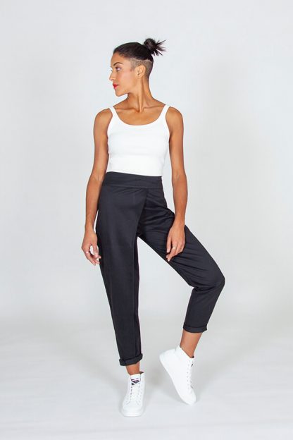 Woman wearing the Panoramix Trousers sewing pattern from I AM Patterns on The Fold Line. A trouser pattern made in lightweight denim, linen, wax, lightweight twill, lightweight gabardine, double gauze, lightweight jacquard, or wool blend fabrics, featuring an ankle length, high waisted, tapered leg with turn-up, waist facing, side invisible zip, back welt pockets and asymmetrical front wrap.
