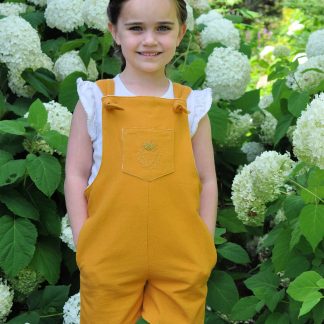 Child wearing the Baby/Child Tipa Dungarees sewing pattern by Below the Kowhai. A sleeveless dress pattern made in light to medium weight cotton, chambray, linen, or medium to heavy weight denim, drill or twill fabrics, featuring cross over back straps and side and front pockets.