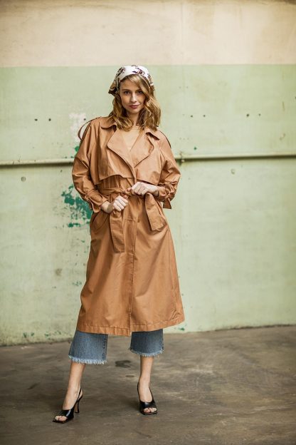 Woman wearing the Martha Trench Coat sewing pattern from Fibre Mood on The Fold Line. A trench coat pattern made in gabardine fabrics, featuring an oversized fit, double breasted front, belted waist, front and back rain flaps, back slit, welt pockets, shoulder lapels and below knee length hem.