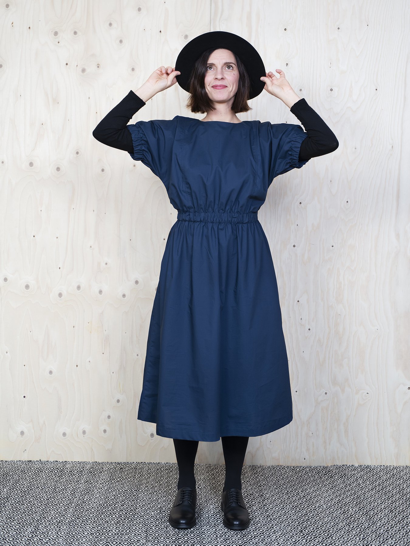 Woman wearing the Cuff Dress sewing pattern from The Assembly Line on The Fold Line. A dress pattern made in cotton, silk, lawn, linen, crepe de chine or wool crepe fabrics, featuring a mid-length finish, relaxed fit, round neck with keyhole opening in the back, side pockets, elastic waist and cap sleeves with elasticated cuffs.