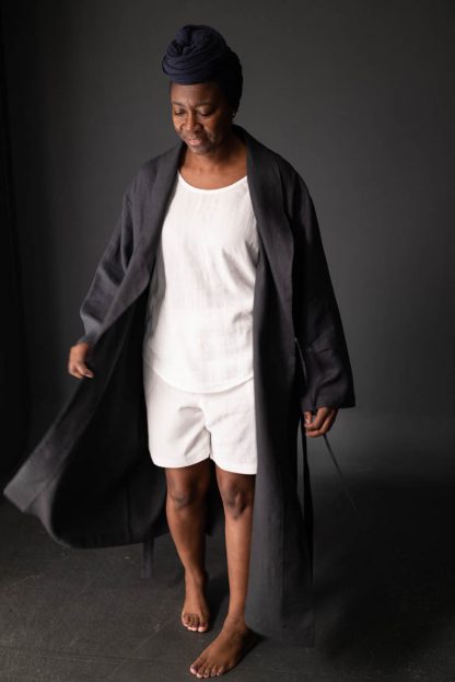 Woman wearing the Unisex Sunday Robe sewing pattern by Merchant and Mills. A robe pattern made in linen, cotton, cotton voile, linen waffle or tencel fabric featuring a loose fit, shawl collar, long length, patch pockets and waist tie.