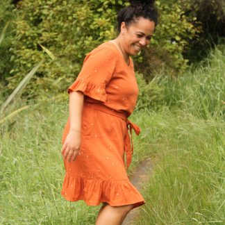 Woman wearing the Pōhutukawa Dress sewing pattern by Below the Kowhai. A shift style dress pattern made in light to medium weight cotton, chambray, poly cotton, linen, rayon, sateen or tencel fabrics, featuring short sleeves, hem ruffle, inseam pockets, and waist tie.