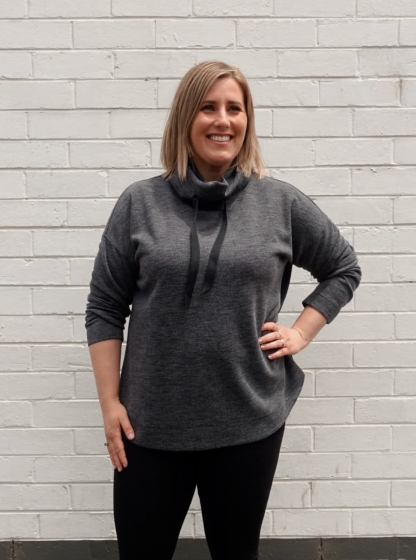 Woman wearing the Verity Knit Top sewing pattern from Style Arc on The Fold Line. A top pattern made in sweater knit, rugby or fleece fabrics, featuring a funnel neck with drawstring, extended shoulder line, boxy shape, slimline long sleeves, slightly scooped hemline with facing and topstitching.