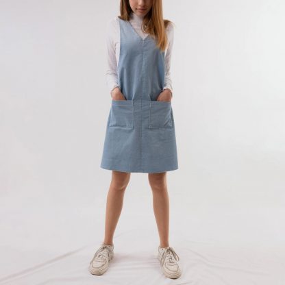 Woman wearing the Katy Pinafore Dress sewing pattern by Fieldwork Patterns. A pinafore dress pattern made in denim, corduroy, heavyweight cottons, gabardine and linen fabrics, featuring patch pockets and a cross over back detail.
