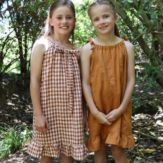 Children wearing the Baby/Child Kororā Dress sewing pattern by Below the Kowhai. A sleeveless dress pattern made in light to medium weight cotton, chambray, lawn, linen, rayon, viscose or voile fabrics, featuring a halter neck and shoulder ties, plus a ruffle hem.