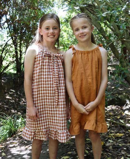 Children wearing the Baby/Child Kororā Dress sewing pattern by Below the Kowhai. A sleeveless dress pattern made in light to medium weight cotton, chambray, lawn, linen, rayon, viscose or voile fabrics, featuring a halter neck and shoulder ties, plus a ruffle hem.