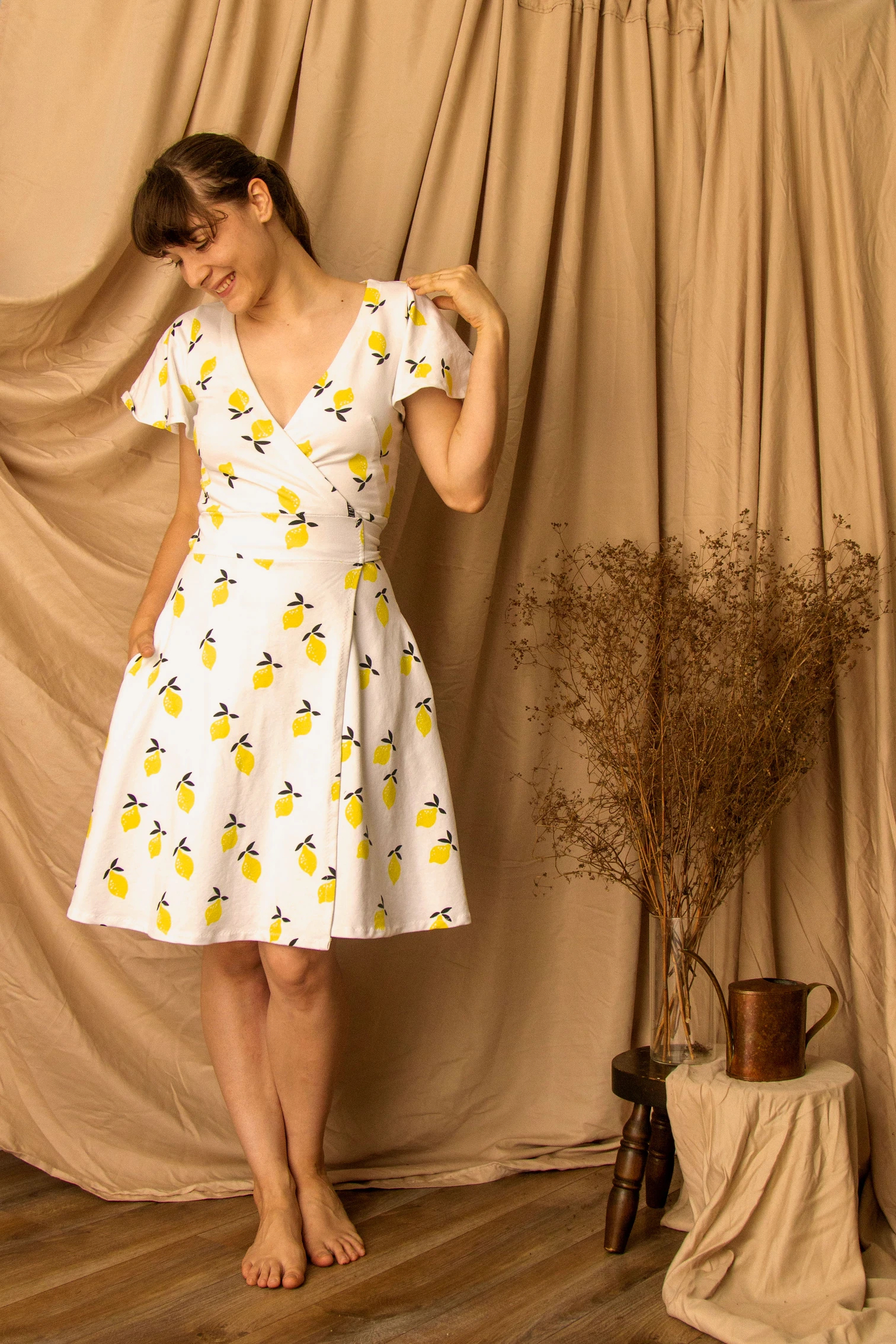 Woman wearing the Mathilde Wrap Dress sewing pattern from Untitled Thoughts on The Fold Line. A wrap dress pattern made in knit fabrics, featuring a back waist tie, V-neck, short flutter sleeves, French darts, in-seam pockets and knee length finish.