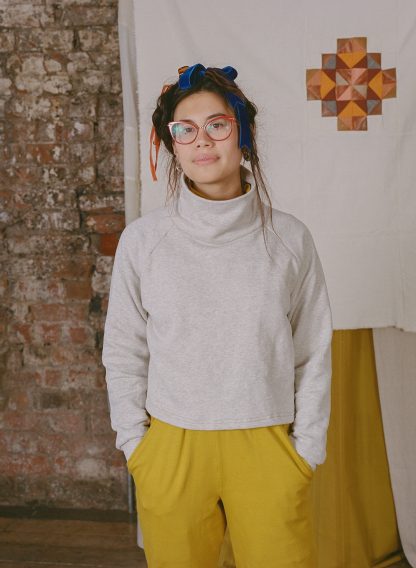 Woman wearing the Zahra Jumper sewing pattern from Made My Wardrobe on The Fold Line. A jumper pattern made in heavy weight knit fabrics, featuring a loose fit, raglan sleeves, cropped length and a high funnel neck.