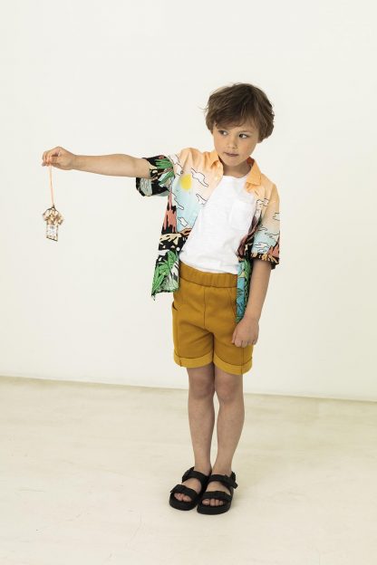 Child wearing the Child/Teen Adam Shorts sewing pattern from Fibre Mood on The Fold Line. A shorts pattern made in woven or knit fabrics, featuring an elasticated waist, turn-up hems, front pockets and relaxed fit.