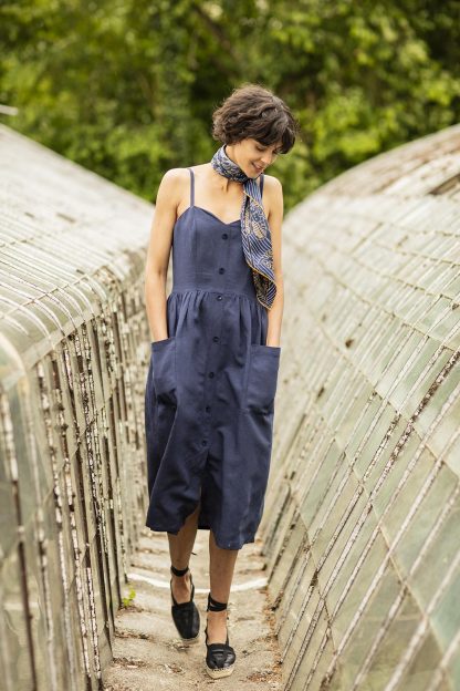 Woman wearing the Colette Dress sewing pattern from Fibre Mood on The Fold Line. A dress pattern made in cotton, denim, linen, viscose (crepe), polyester (crepe) or Tencel fabrics, featuring a button front, side invisible zip, raised waist, fitted top with spaghetti straps, patch pockets, A-line skirt with front slit.