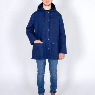 Man wearing the Men's Jacques Raincoat sewing pattern from I AM Patterns on The Fold Line. A raincoat pattern made in water-resistant and waterproof fabrics, gabardine, waxed cotton, wool coating, cotton serge, cotton twill, denim or corduroy fabrics, featuring a hood, zipper hidden by a placket which closes with snap fasteners, two big patch pockets and fully lined.