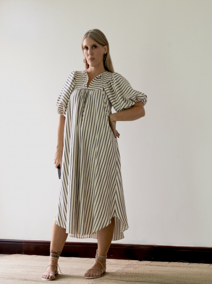 Woman wearing the Vali Dress sewing pattern from Pattern Fantastique on The Fold Line. A dress pattern made in viscose, silks, linen or cotton fabrics, featuring a high round neck with narrow V front opening with tie, sleeve and yoke gathers, topstitched facings, in-seam pocket, high low hem, midi length, elbow length sleeves.