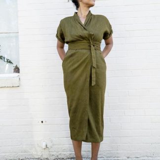 Woman wearing the Wildwood Wrap Dress sewing pattern from Sew House Seven on The Fold Line. A wrap dress pattern made in linen blends, cotton lawn, dress weight cottons, rayon or silk fabrics, featuring a shawl collar, waist and shoulder pleats, front slash pockets, slim fitting skirt, grown on short sleeves, below knee length and self-fabric waist tie.