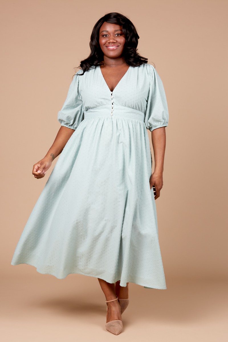 Woman wearing the Orchidée Dress sewing pattern by Deer and Doe. A dress pattern made in batiste, cotton voile, swiss dots or eyelet fabrics, featuring a deep V-neck, bridal buttons, zipper closure, elbow length puff sleeves, full skirt and deep waistband.