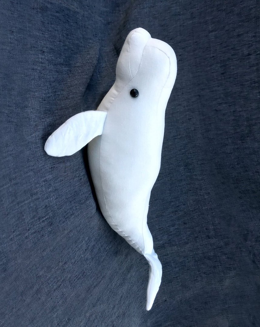Image showing the Beluga Whale Soft Toy sewing pattern from Crafty Kooka on The Fold Line. A soft toy pattern made in any sort of cream or white fabric, featuring a black beady eye, cheeky smile, bulbous head, flippers and tail fin.