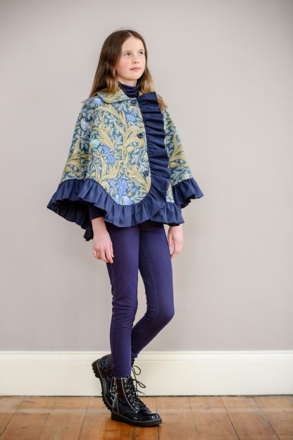 Child wearing the Children's Stornoway Cape sewing pattern by Greyfriars and Grace. A cape pattern made in mid-heavy weight wool, cotton, linen or cotton/linen blend fabric for cape and cotton lining, featuring a front button closure, collar and ruffle hem.