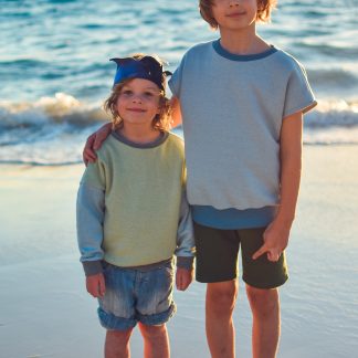 Children wearing the Baby/Child Driftwood Dolman Sweatshirt sewing pattern from Waves and Wild on The Fold Line. A sweatshirt pattern made in medium-weight knit fabric, featuring a relaxed fit, short or long sleeves, round neck and ribbing to the cuff and waist.