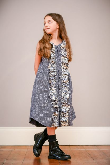 Child wearing the Shirt to Children's Finnieston Dress sewing pattern by Greyfriars and Grace. A sleeveless dress pattern made in pre-loved shirt fabrics, featuring a relaxed fit, front button closure with ruffle and gathered waist.