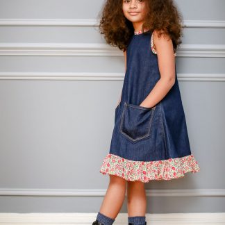 Child wearing the Jeans to Children's Joppa Dress sewing pattern by Greyfriars and Grace. A sleeveless dress pattern made in pre-loved denim fabrics, featuring an A-line silhouette, front pockets, hem ruffle and contrasting bias binding on the neckline, back neck tie and armholes.