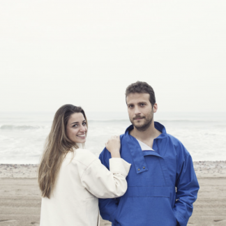 Man and women wearing the Unisex Maritims Pullover sewing pattern by Pauline Alice. A cagoule pattern made in cotton canvas, denim, gabardine, corduroy or nylon fabrics, featuring a large front pocket, high collar with zipped opening, interior pocket, adjustable hem with drawstrings and cuffed sleeves.