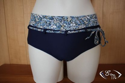 Mannequin wearing the Neptune Swimsuit Bottoms sewing pattern from Etoffe Malicieuse on The Fold Line. A bikini bottom pattern made in swimsuit fabrics, featuring a low rise leg, full coverage, and a belt with left sided tie.