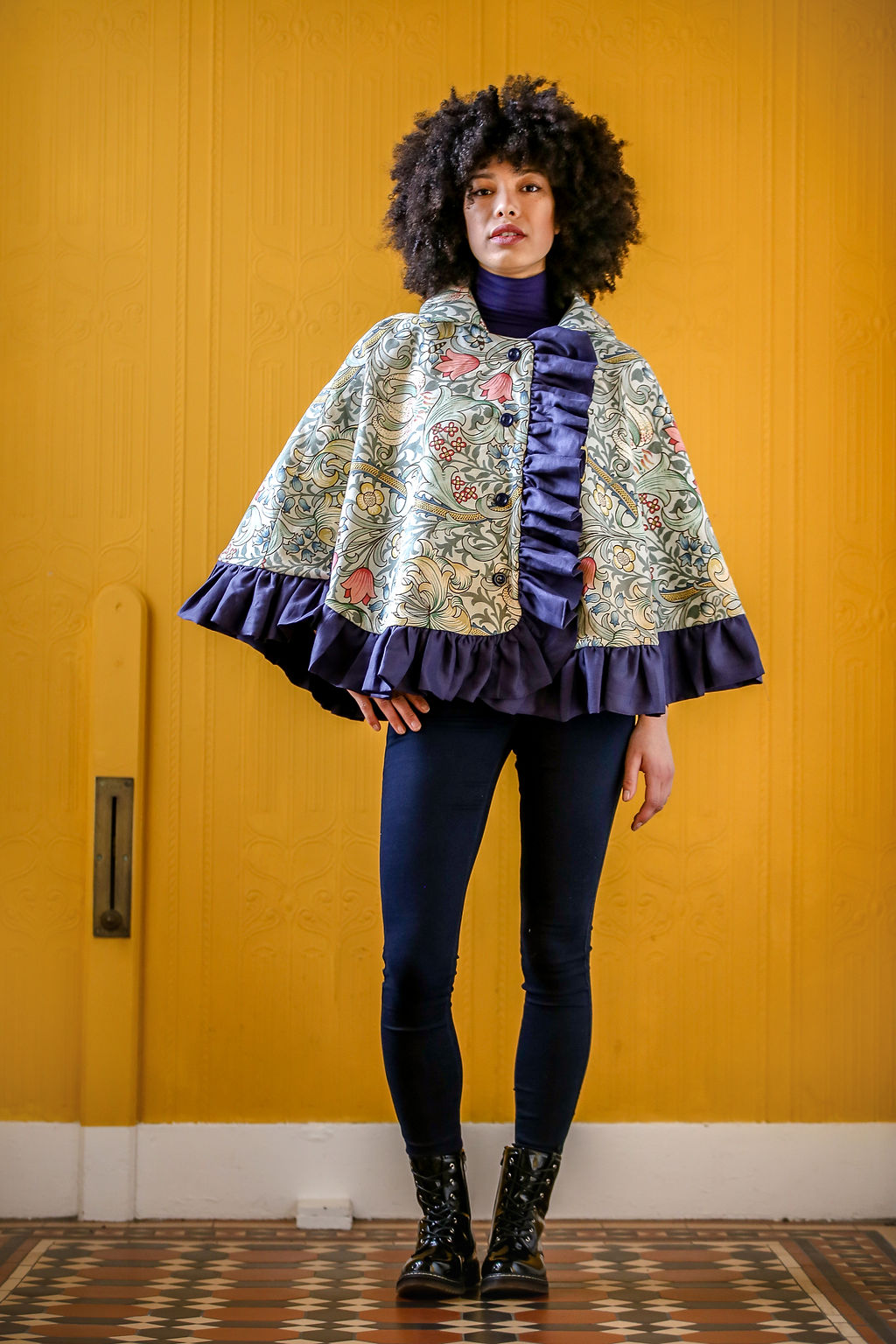 Woman wearing the Stornoway Cape sewing pattern by Greyfriars and Grace. A cape pattern made in mid-heavy weight wool, cotton, linen or cotton/linen blend fabric for cape and cotton lining, featuring a front button closure, collar and ruffle hem.