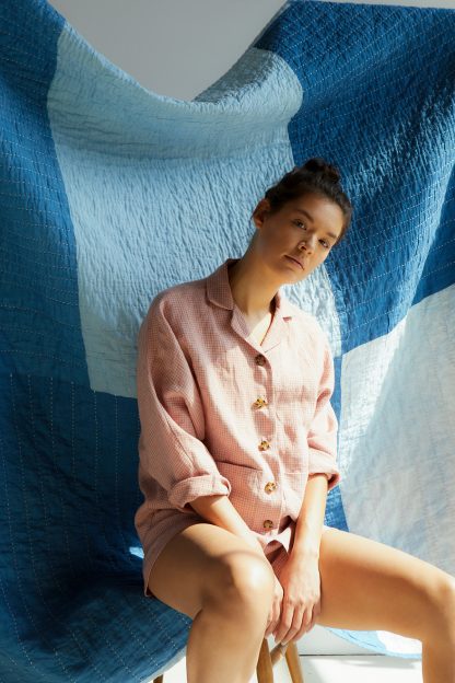 Woman wearing the Agnes Pyjama Set pattern from Paper Theory Patterns on The Fold Line. A PJ pattern made in cotton lawn, poplin, linen, cotton voile, double gauze or soft denim fabrics, featuring shorts with high waist and elasticated waistband, the shirt has button front closure, patch pockets, relaxed fit, batwing sleeves and collar.