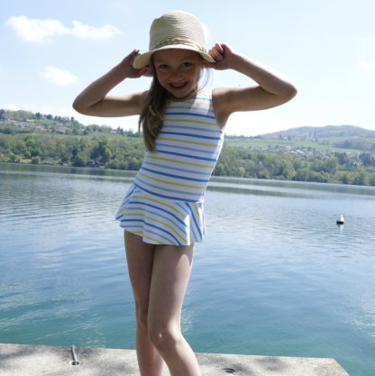 Child wearing the Child/Teen Bahia Swimsuit sewing pattern from Petits D’om on The Fold Line. A swimsuit pattern made in swimsuit fabrics, featuring a round neckline, broad shoulder straps and ruffle skirt.