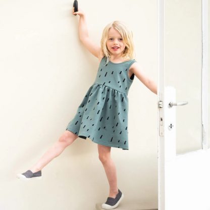Child wearing the Child/Teen Jente Dress sewing pattern from Itch to Stitch on The Fold Line. A sleeveless dress pattern made in stretch fabrics such as tencel or bamboo jersey, featuring a gathered skirt, overlapping back panels with a low cut and boat neckline.