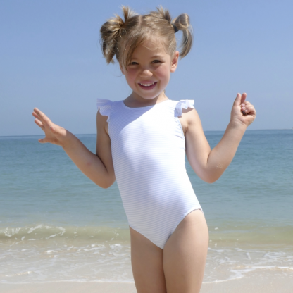 Child wearing the Child/Teen Olita Swimsuit sewing pattern from Petits D’om on The Fold Line. A swimsuit pattern made in swimsuit fabrics, featuring a round neck, lower at the back than front and embellished with a ruffle.