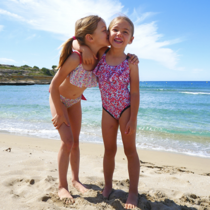 Children wearing the Child/Teen Ouvéa Swimsuit sewing pattern from Petits D’om on The Fold Line. A swimsuit or bikini pattern made in swimsuit fabrics, featuring a top with wide ruffle, thin shoulder straps, the bikini bottom has tied knot fastenings.