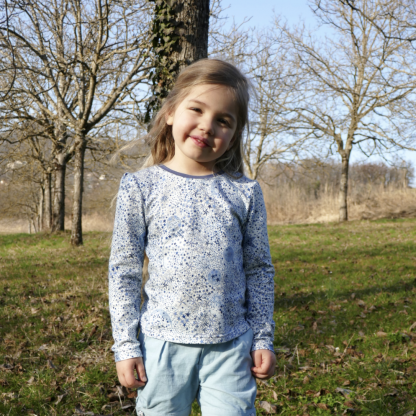 Child wearing the Child/Teen Siloé Polo or T-shirt sewing pattern from Petits D’om on The Fold Line. A top pattern made in jersey fabrics, featuring a round neck with contrast band, long sleeves with shoulder gathers.