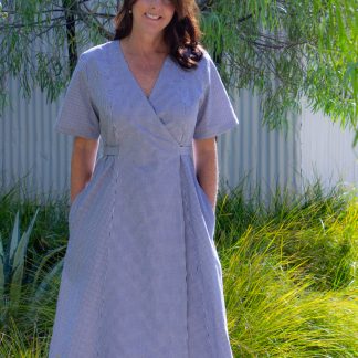 Woman wearing the Andrea Wrap Dress sewing pattern from Blue Dot Patterns on The Fold Line. A wrap dress pattern made in chambray, light to medium weight cottons, lightweight linen, poplin, lightweight denim, crepe or challis fabrics, featuring a loose fitting, princess seams, set-in sleeves, front and back yoke. The waist tie sits 1" above the waist, midi length, in-seam pockets and short sleeves.