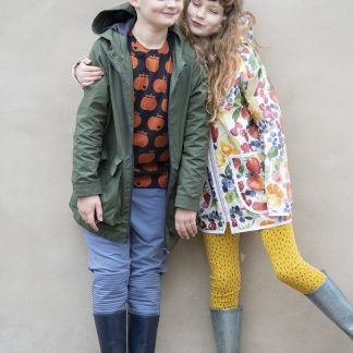 Children wearing the David Raincoat sewing pattern from Bobbins and Buttons on The Fold Line. A unisex raincoat pattern made in laminated cotton, polyurethane, coated cotton, cotton drill or denim fabrics, featuring a zip-front, bound edges, raglan sleeves, panelled hood, big boxy pockets or pockets with flaps.